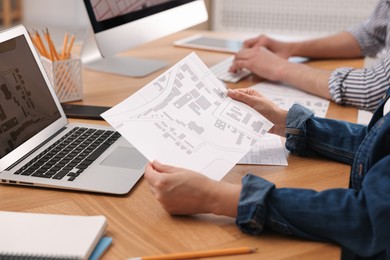 Photo of Cartographer working with cadastral map at wooden table, closeup