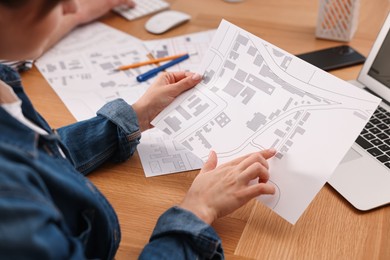 Photo of Cartographer working with cadastral map at wooden table, closeup