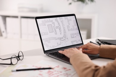 Cartographer working with cadastral map on laptop at white table in office, closeup