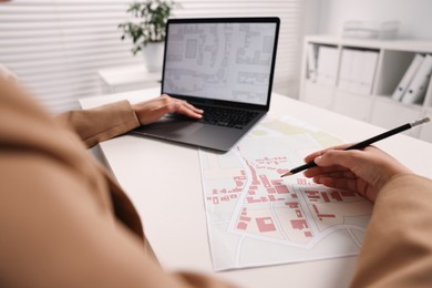 Cartographer working with cadastral map on laptop at white table in office, closeup