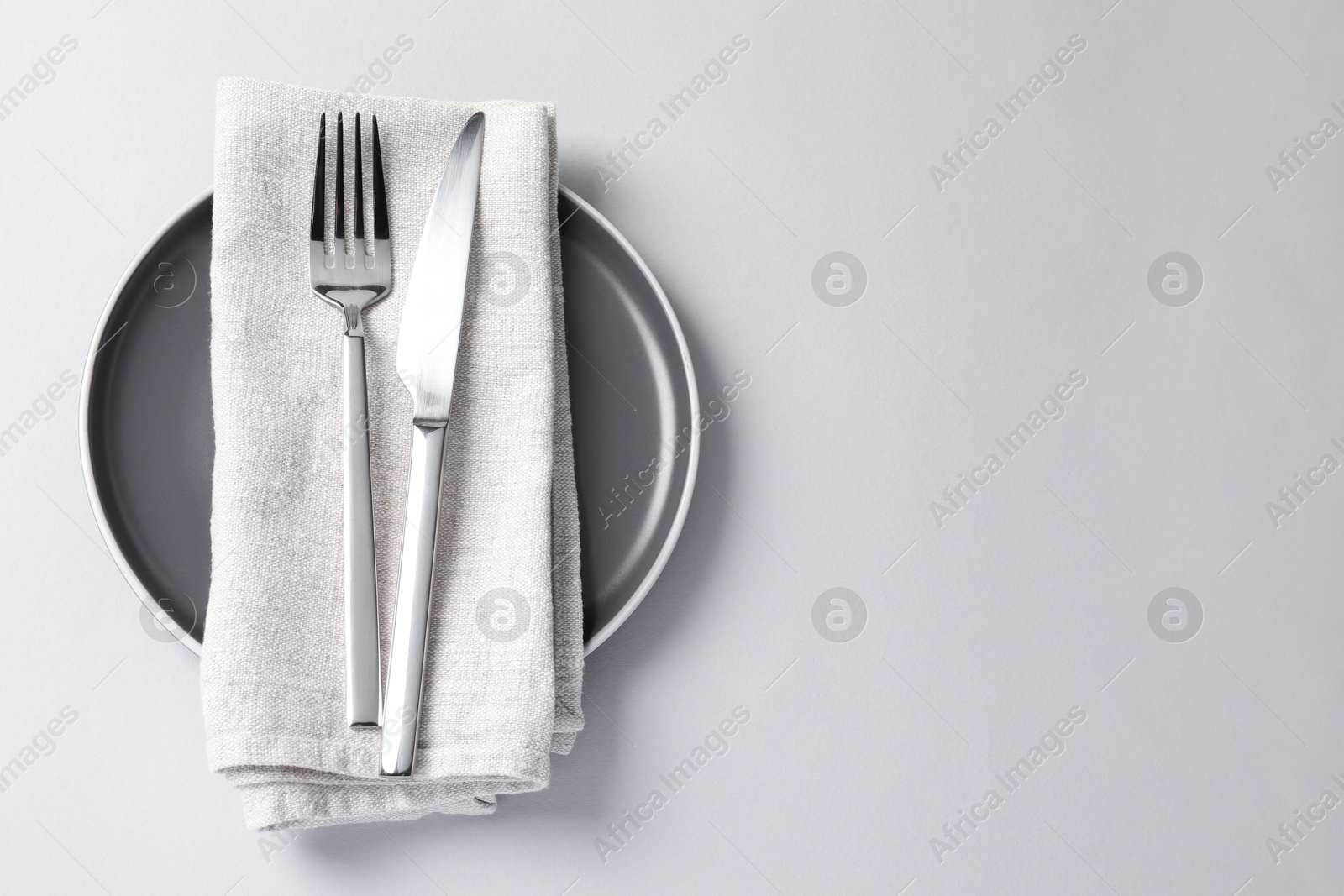 Photo of Stylish silver cutlery, plate and napkin on white background, top view. Space for text