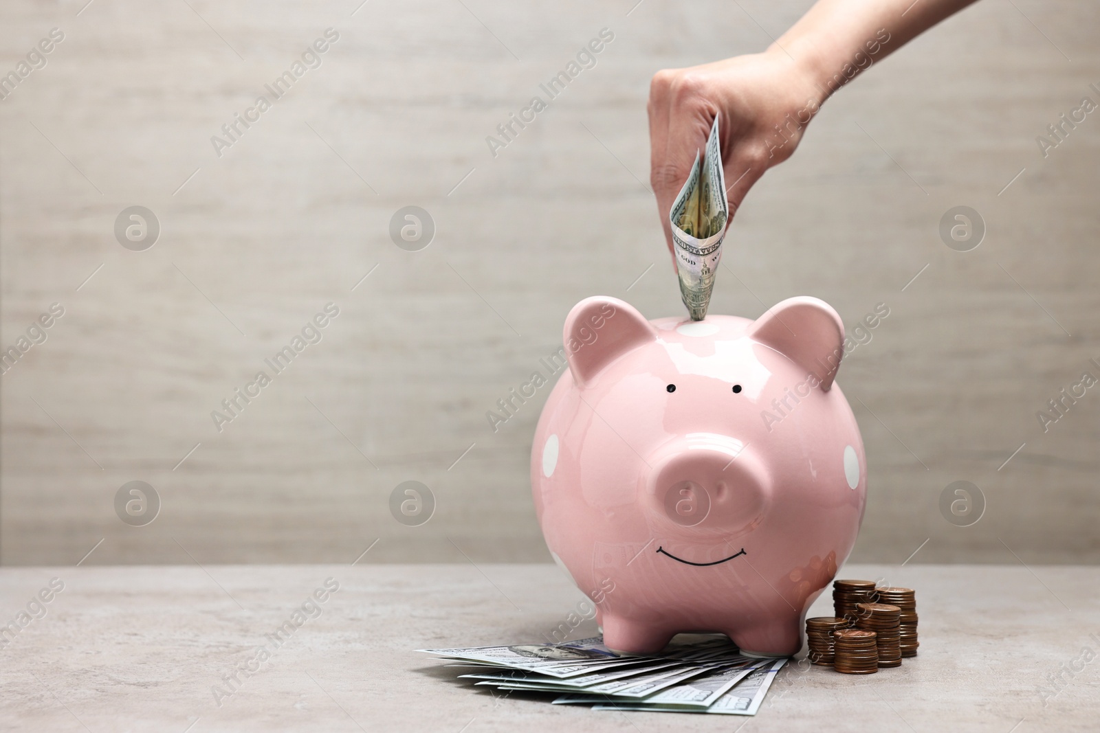 Photo of Woman putting dollar banknote into pink piggy bank at grey table, closeup. Space for text