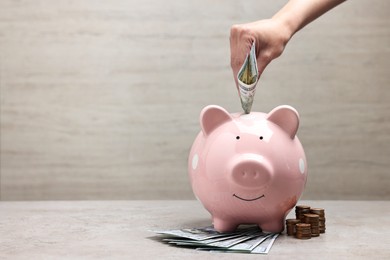 Photo of Woman putting dollar banknote into pink piggy bank at grey table, closeup. Space for text