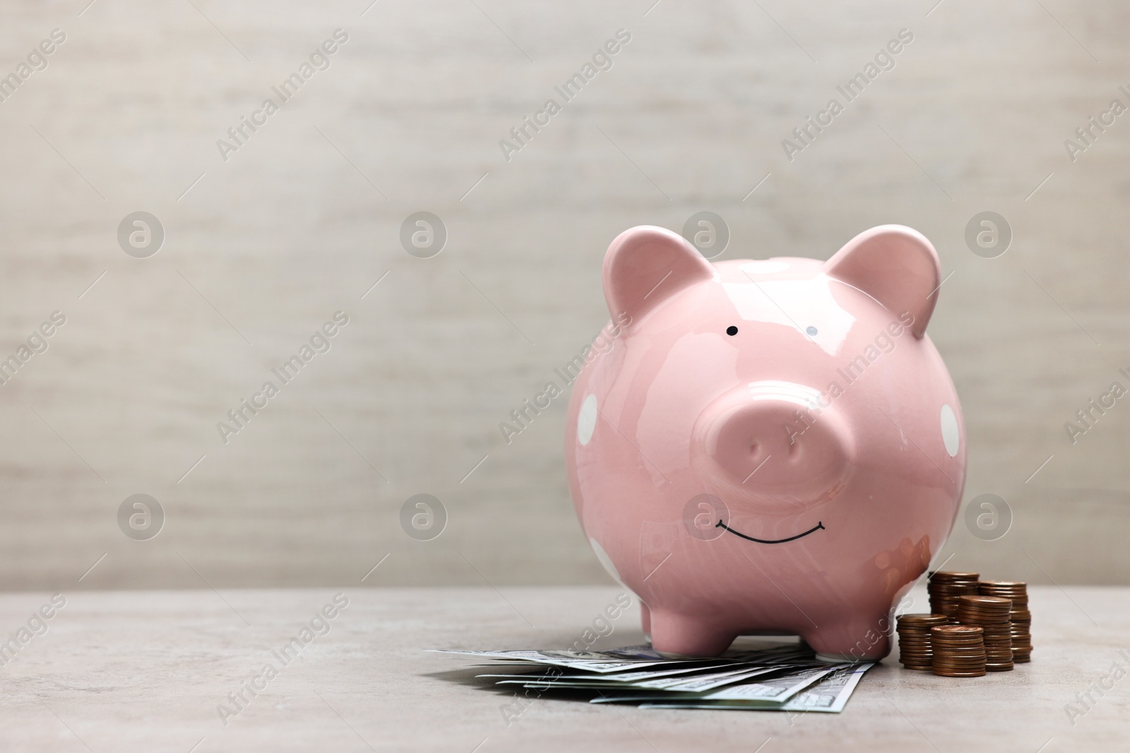 Photo of Pink piggy bank with dollar banknotes and stacks of coins on grey table, space for text