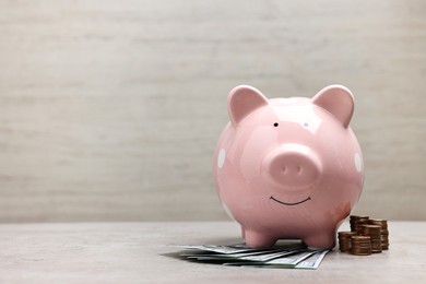 Photo of Pink piggy bank with dollar banknotes and stacks of coins on grey table, space for text