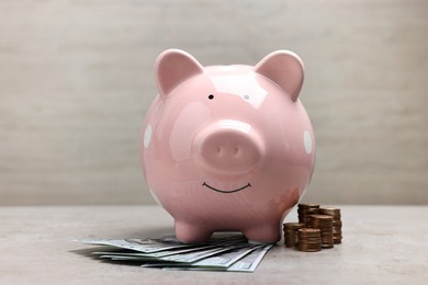 Pink piggy bank with dollar banknotes and stacks of coins on grey table