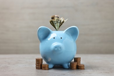 Light blue piggy bank with dollar banknotes and stacks of coins on grey table