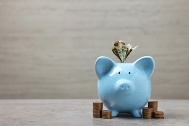 Light blue piggy bank with dollar banknotes and stacks of coins on grey table, space for text