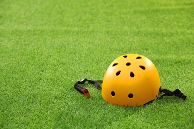 Yellow protective helmet on green grass, space for text