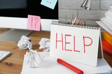 Photo of Notebook with word Help, computer and stationery on wooden table at workplace