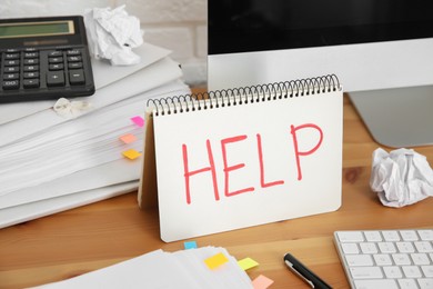 Notebook with word Help, computer and stationery on wooden table at workplace