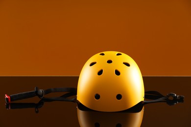 Photo of Stylish protective helmet on mirror surface against orange background. Space for text