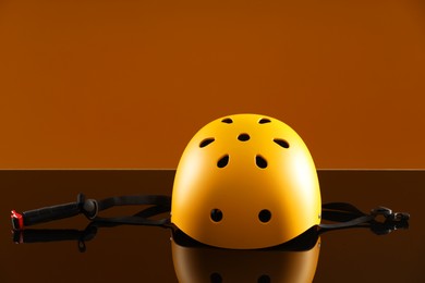 Stylish protective helmet on mirror surface against orange background. Space for text