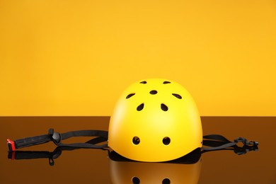 Photo of Stylish protective helmet on mirror surface against orange background. Space for text