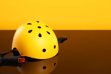 Stylish protective helmet on mirror surface against orange background. Space for text