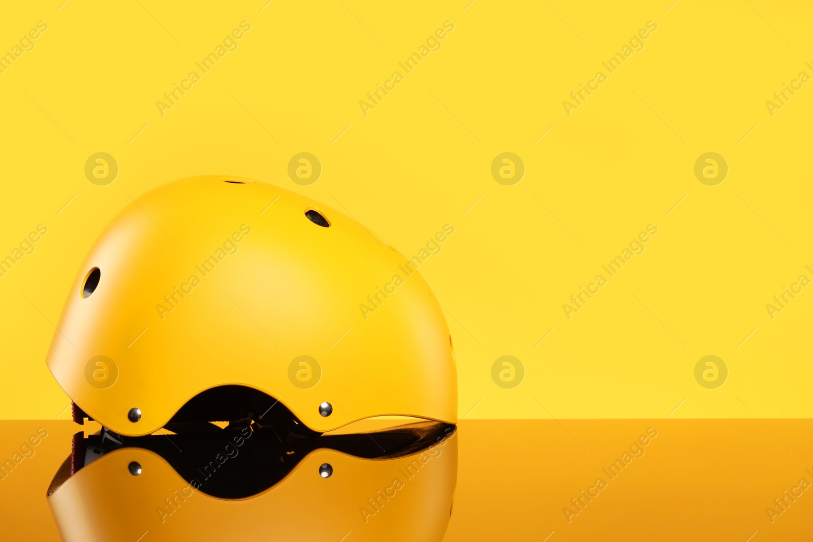 Photo of Stylish protective helmet on mirror surface against yellow background. Space for text