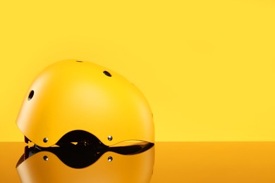 Photo of Stylish protective helmet on mirror surface against yellow background. Space for text