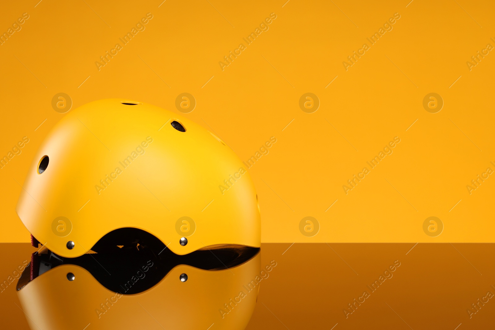 Photo of Stylish protective helmet on mirror surface against yellow background. Space for text