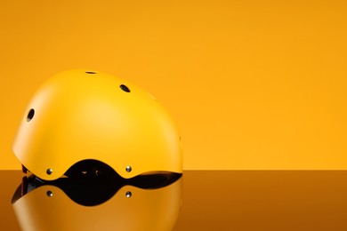 Photo of Stylish protective helmet on mirror surface against yellow background. Space for text