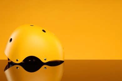 Stylish protective helmet on mirror surface against yellow background. Space for text