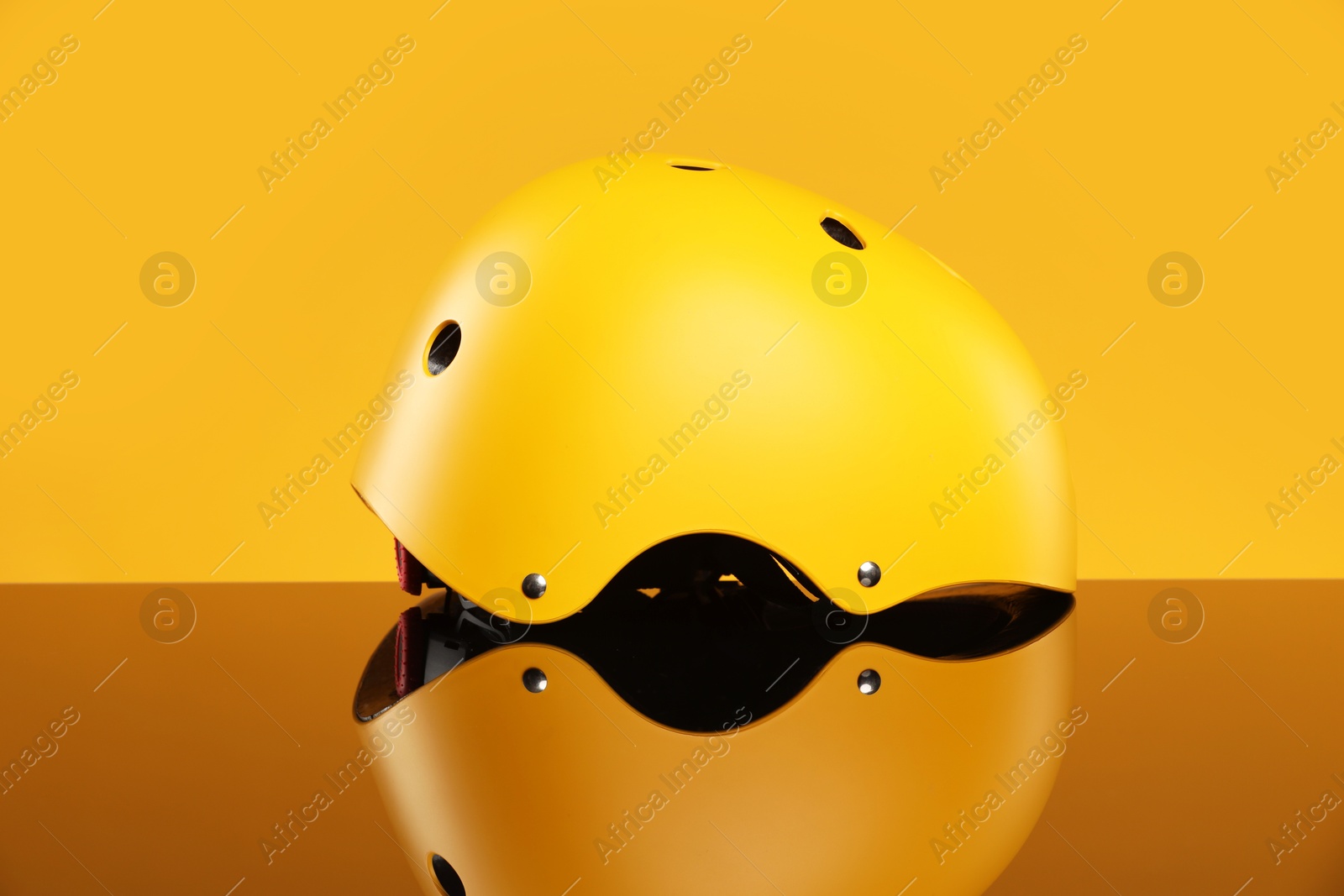 Photo of Stylish protective helmet on mirror surface against yellow background