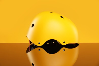 Photo of Stylish protective helmet on mirror surface against yellow background