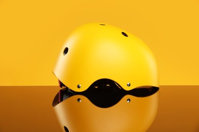 Stylish protective helmet on mirror surface against yellow background