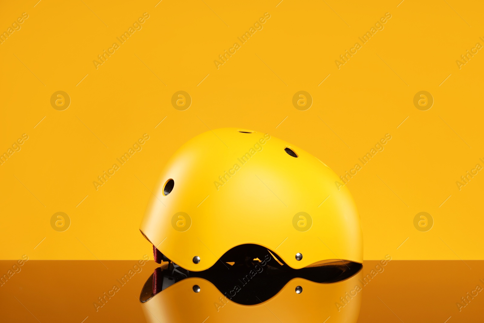 Photo of Stylish protective helmet on mirror surface against yellow background. Space for text