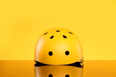 Photo of Stylish protective helmet on mirror surface against yellow background
