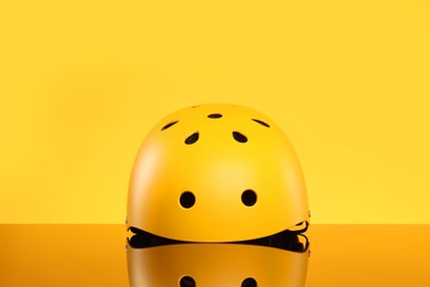 Stylish protective helmet on mirror surface against yellow background