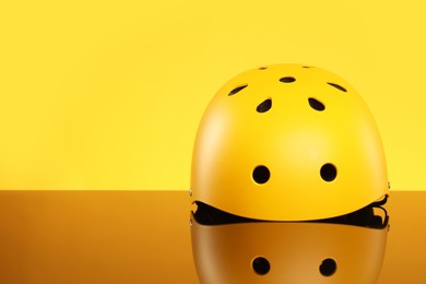 Photo of Stylish protective helmet on mirror surface against yellow background. Space for text