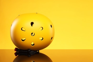 Photo of Stylish protective helmet on mirror surface against yellow background. Space for text