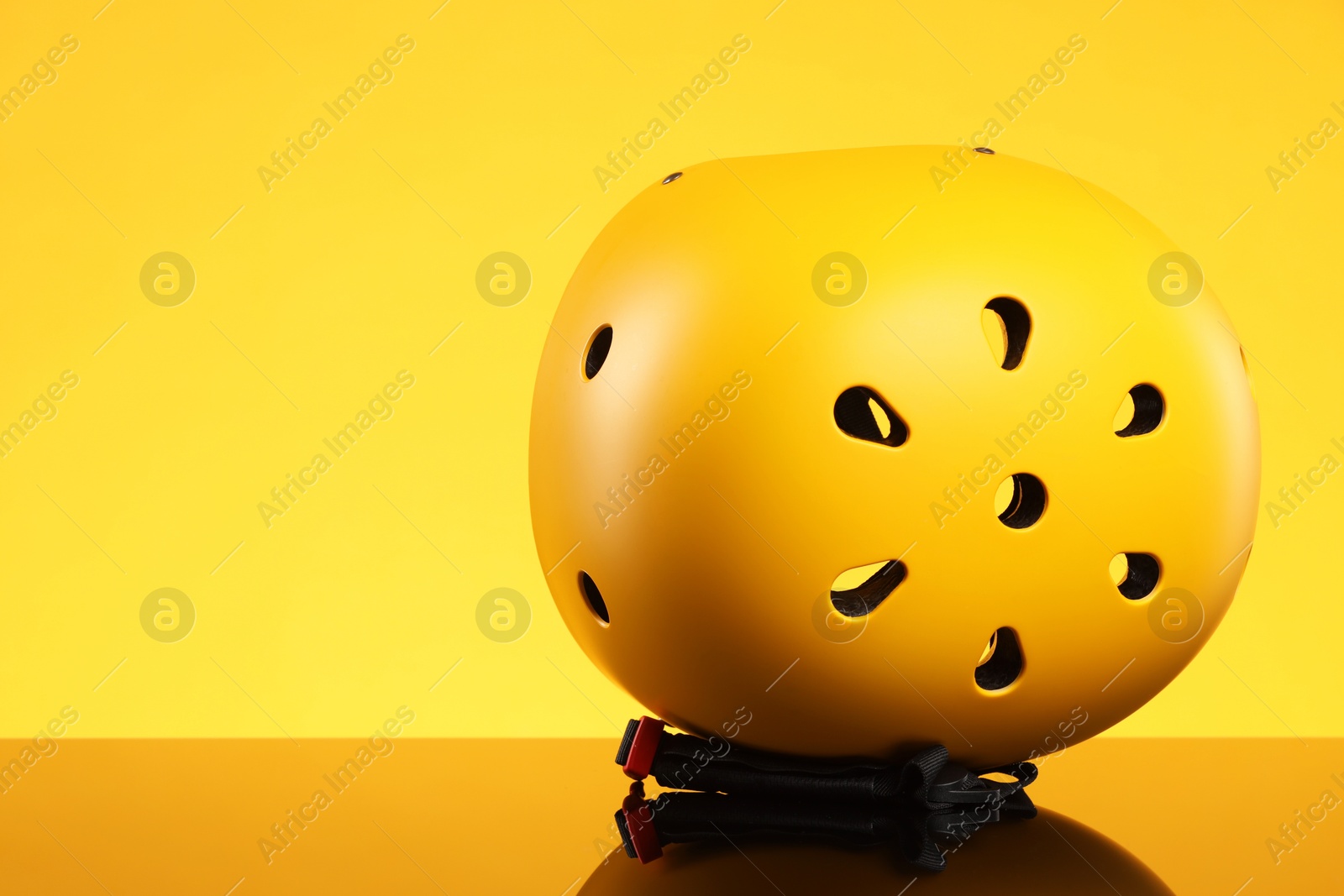 Photo of Stylish protective helmet on mirror surface against yellow background. Space for text