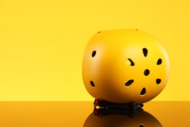 Stylish protective helmet on mirror surface against yellow background. Space for text