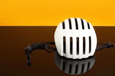 Photo of White protective helmet on mirror surface against orange background. Space for text