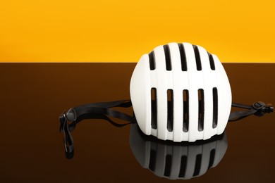 White protective helmet on mirror surface against orange background. Space for text