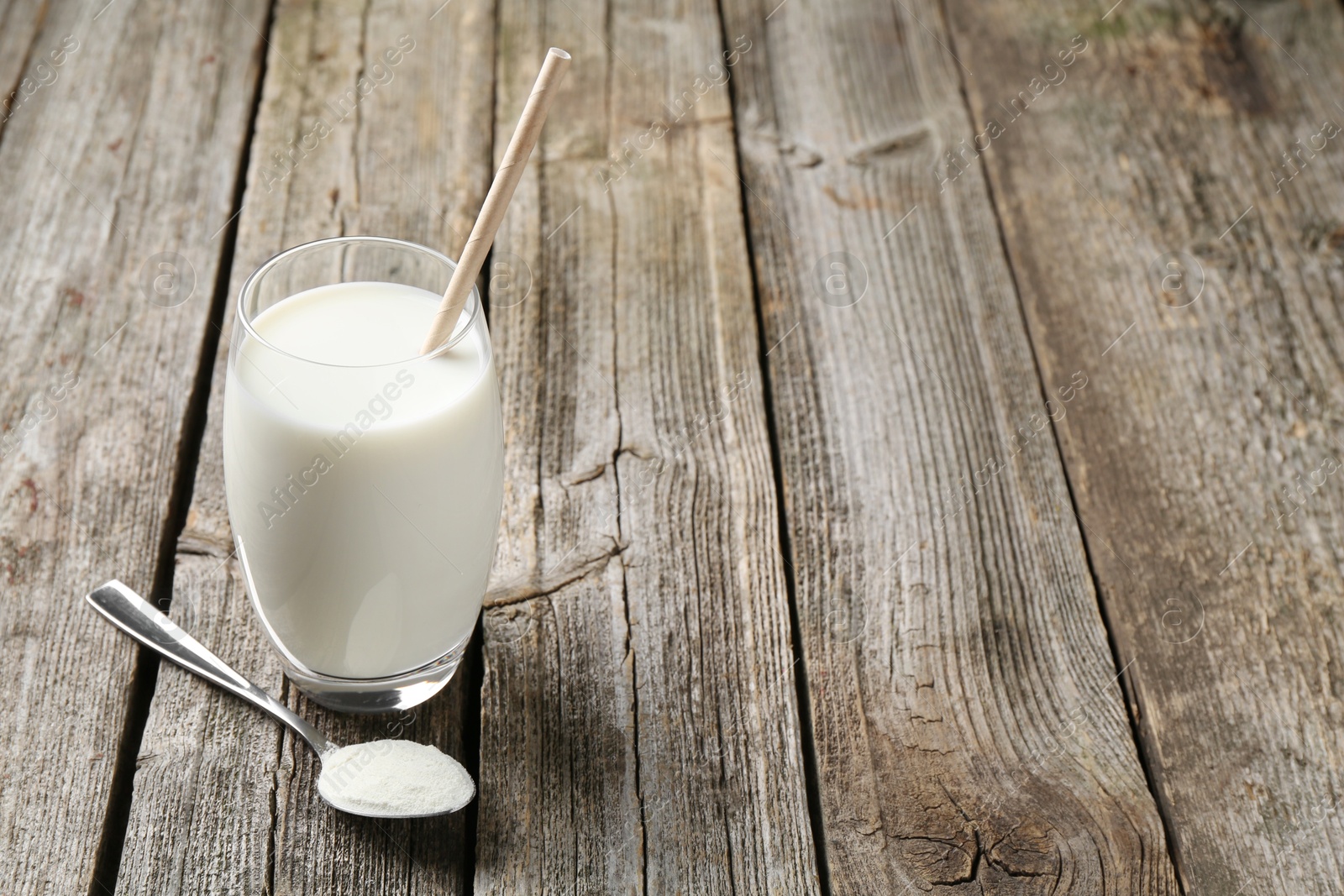 Photo of Delicious protein shake in glass and spoon with powder on wooden table, space for text