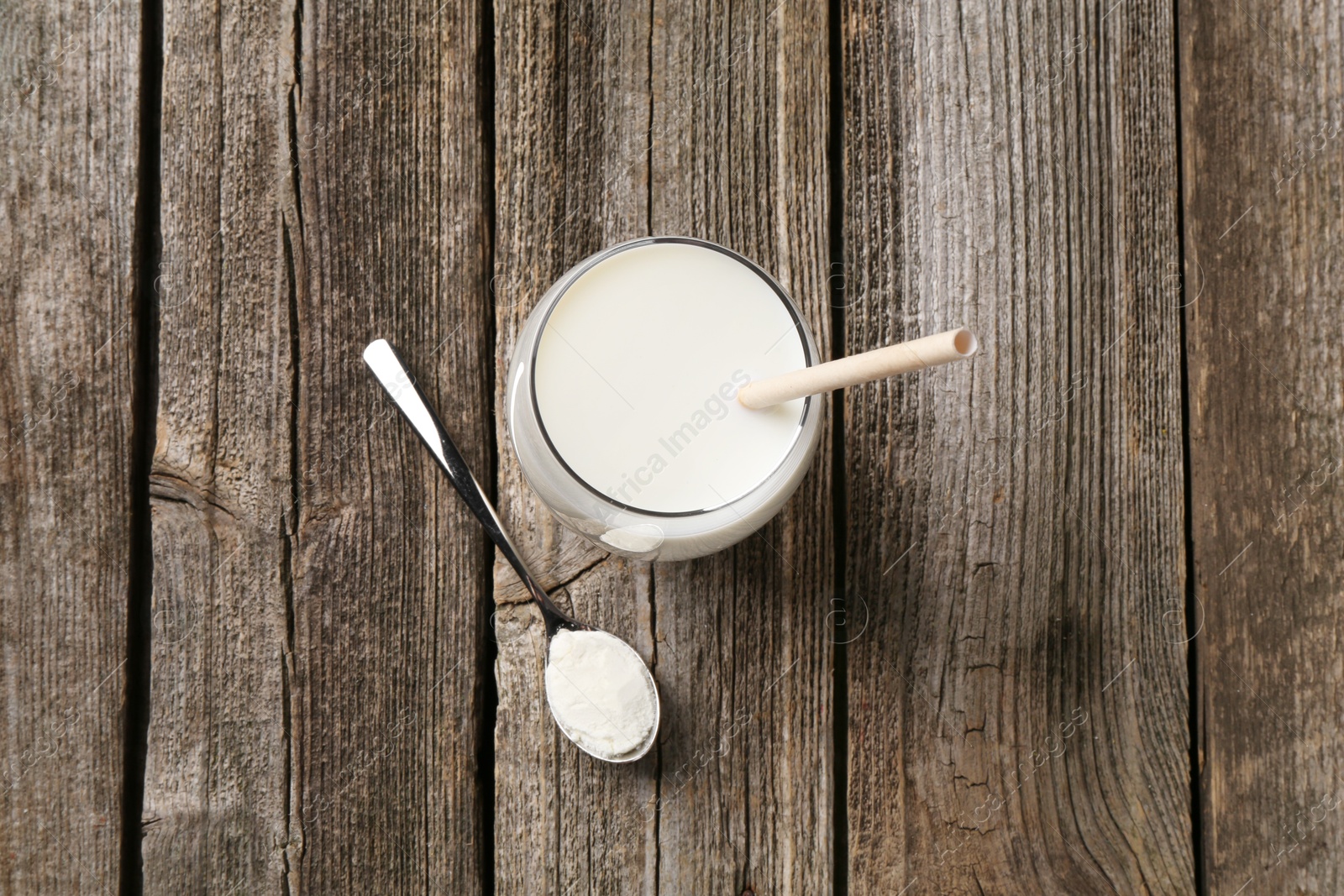 Photo of Delicious protein shake in glass and spoon with powder on wooden table, top view