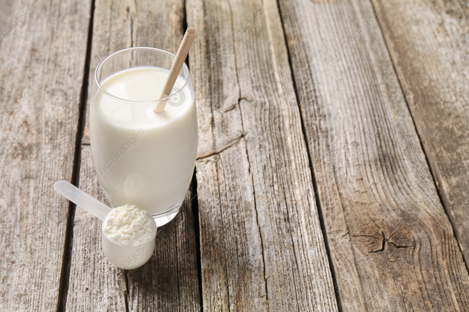 Photo of Delicious protein shake in glass and scoop with powder on wooden table, space for text