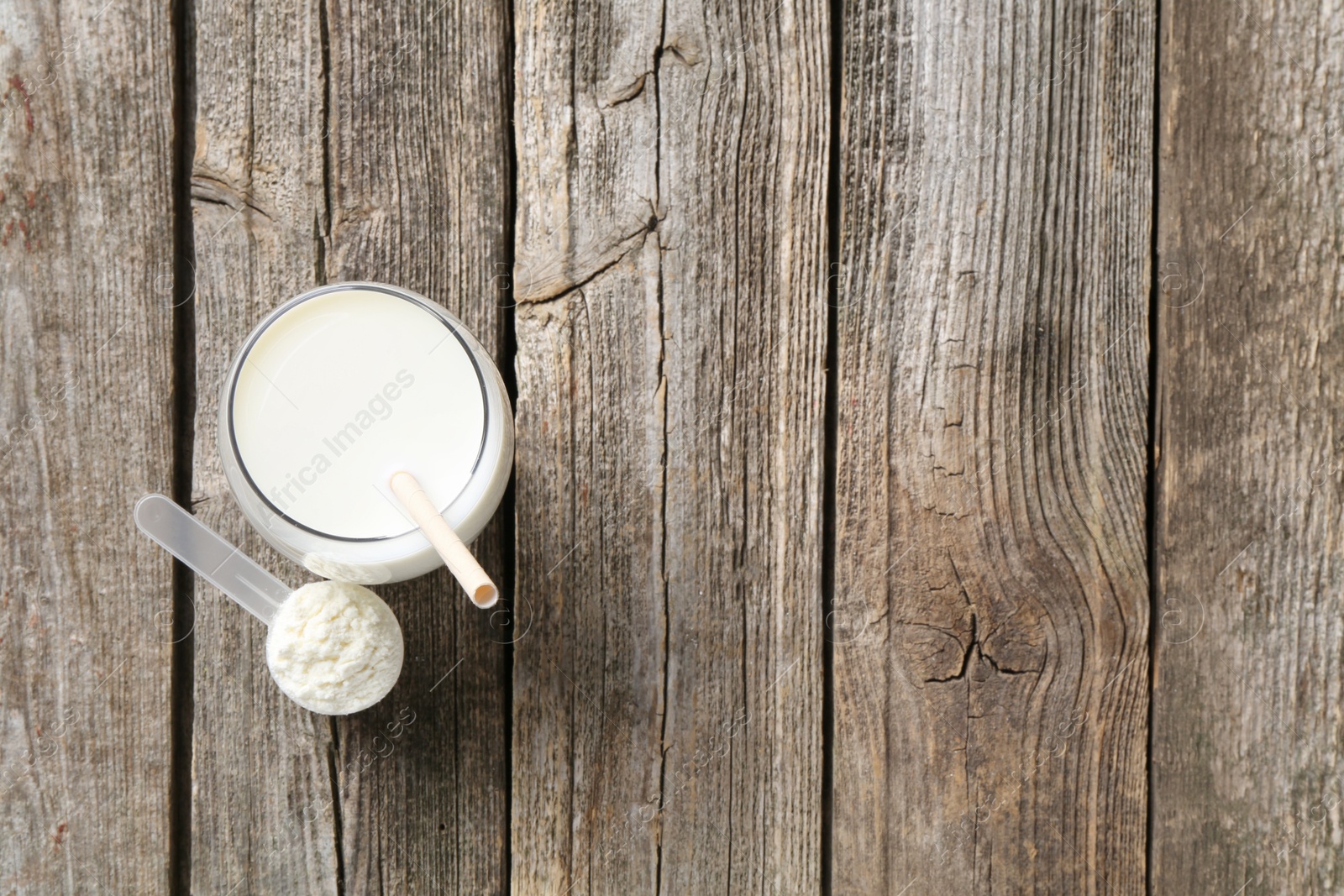 Photo of Delicious protein shake in glass and scoop with powder on wooden table, top view. Space for text