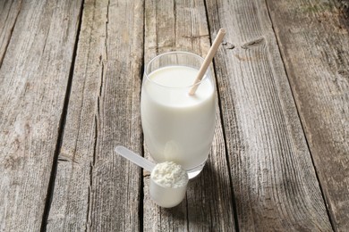 Photo of Delicious protein shake in glass and scoop with powder on wooden table