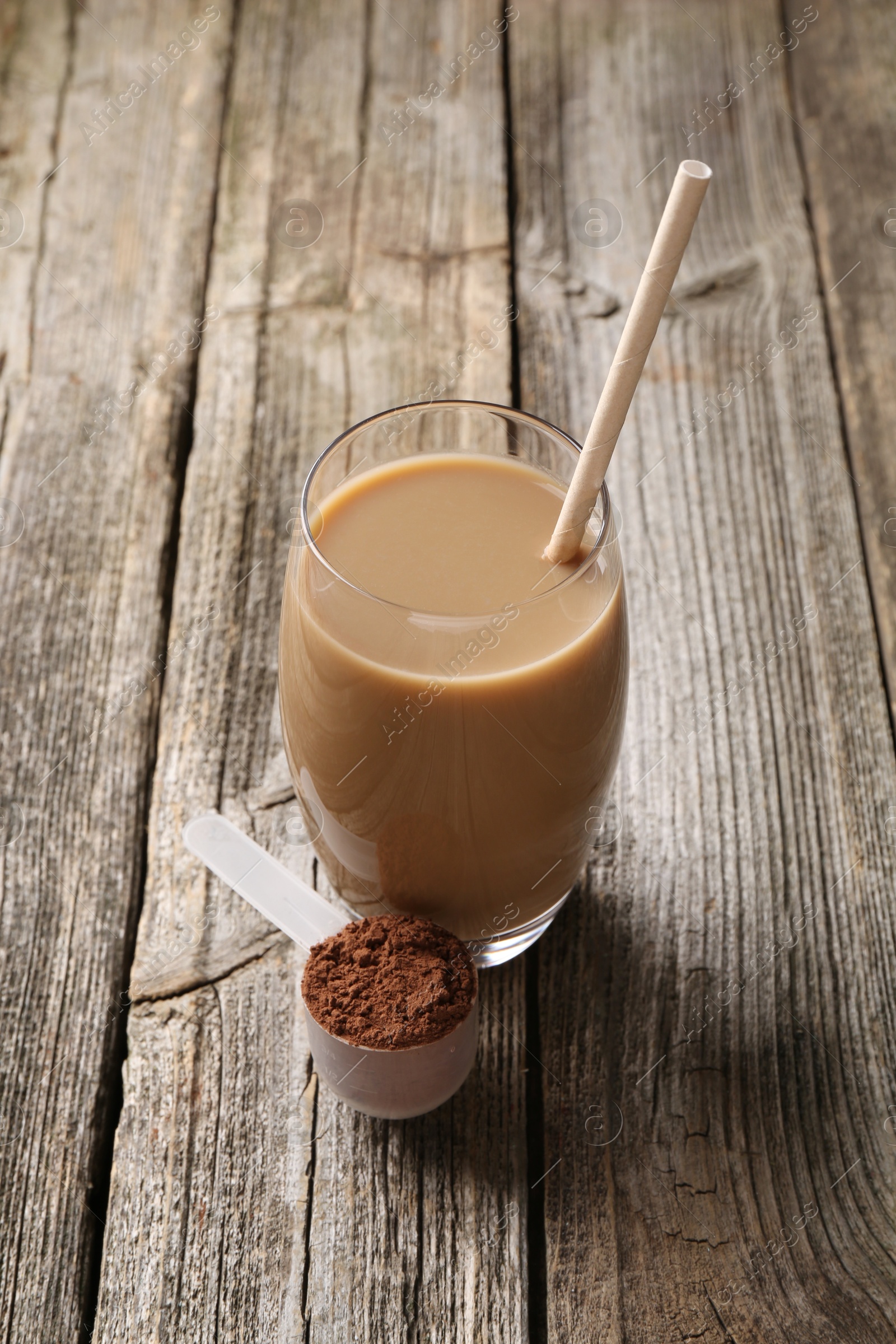 Photo of Delicious protein shake in glass and scoop with powder on wooden table