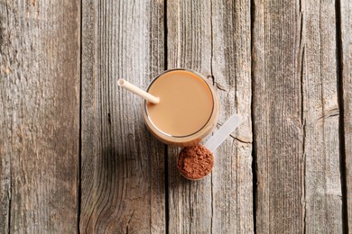 Photo of Delicious protein shake in glass and scoop with powder on wooden table, top view