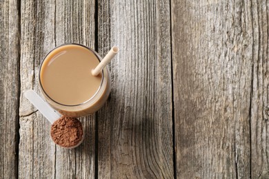 Photo of Delicious protein shake in glass and scoop with powder on wooden table, top view. Space for text