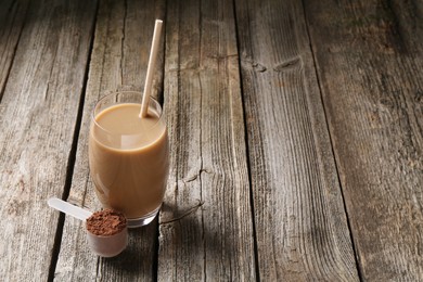 Photo of Delicious protein shake in glass and scoop with powder on wooden table, space for text