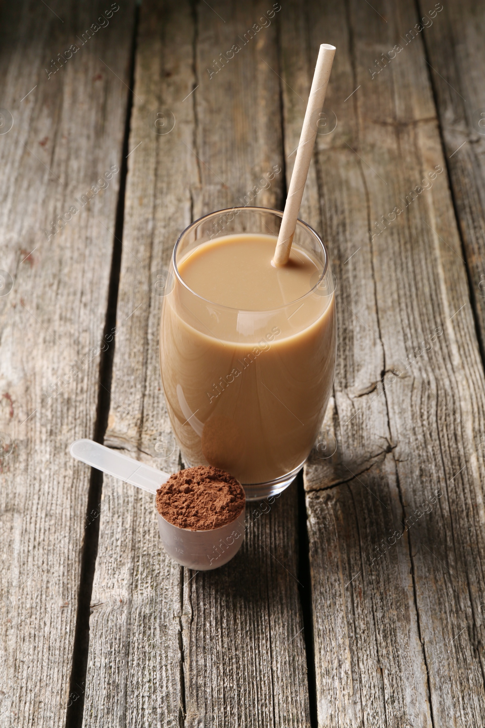 Photo of Delicious protein shake in glass and scoop with powder on wooden table