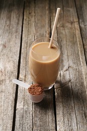 Photo of Delicious protein shake in glass and scoop with powder on wooden table