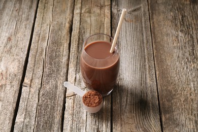 Photo of Delicious protein shake in glass and scoop with powder on wooden table