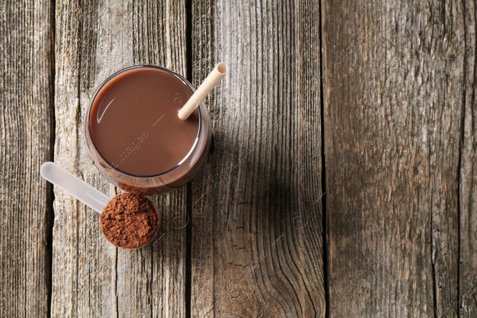 Photo of Delicious protein shake in glass and scoop with powder on wooden table, top view. Space for text