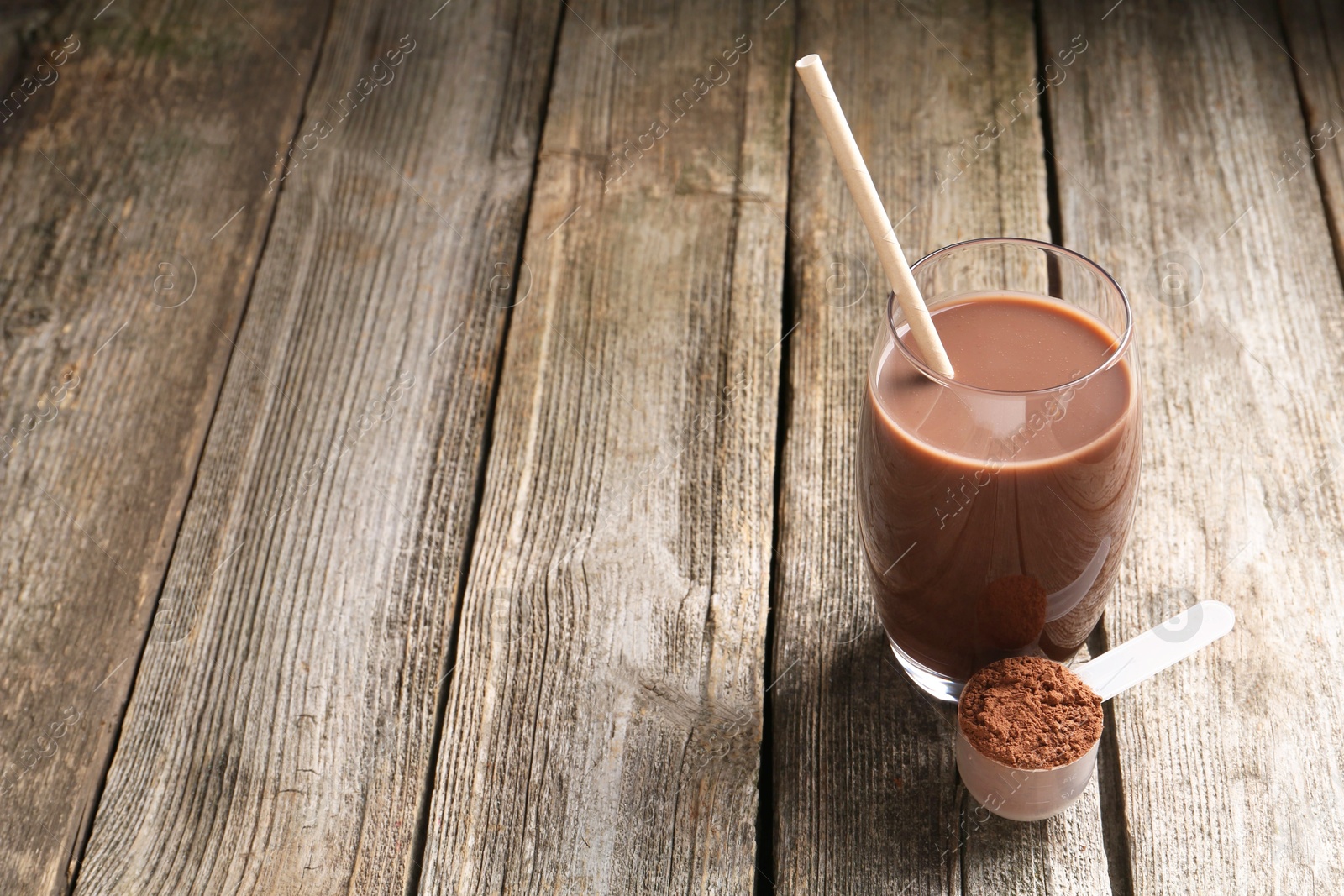 Photo of Delicious protein shake in glass and scoop with powder on wooden table, space for text